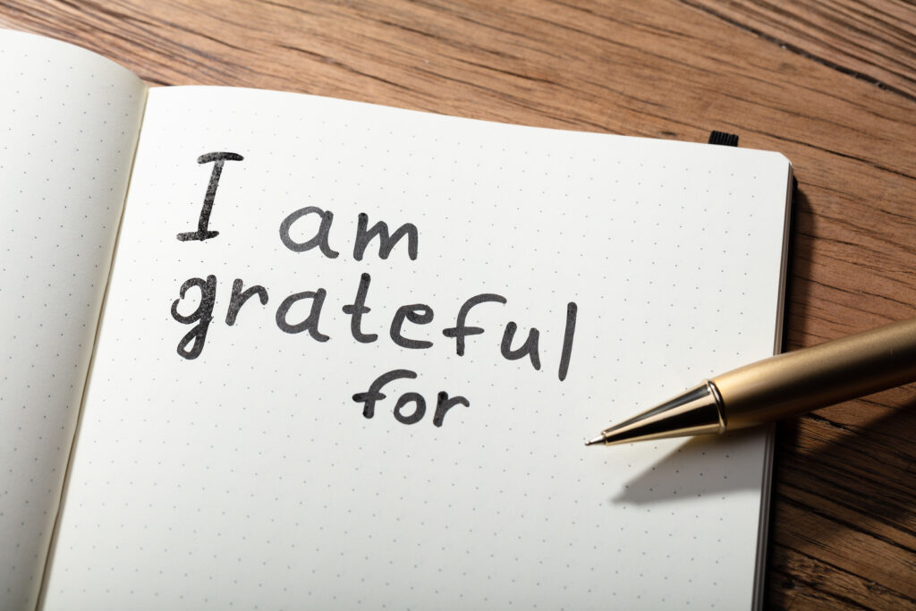 Close-up Of Gratitude Word With Pen On Notebook Over Wooden Desk